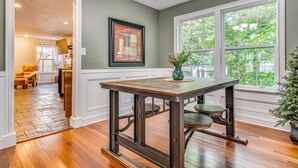 A dining area with a table and chairs, a framed picture on the wall, and a window with a view of greenery. - Treehouse Views! Walking Distance to IMS (Indianapolis)