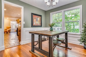 A dining area with a table and chairs, a framed picture on the wall, and a window with a view of greenery. - Treehouse Views! Walking Distance to IMS (Indianapolis)
