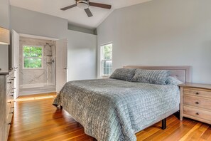 Une chambre à coucher comprenant un lit, une table de chevet, une commode, un dressing, un ventilateur de plafond et une fenêtre.