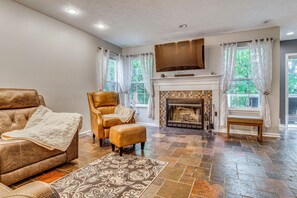 A living room with a fireplace, leather sofa, ottoman, patterned rug, and a large flat-screen TV. - Treehouse Views! Walking Distance to IMS (Indianapolis)