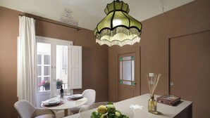 Un coin repas avec une table dressée pour deux personnes, un lustre et une porte ornée d’un panneau décoratif.