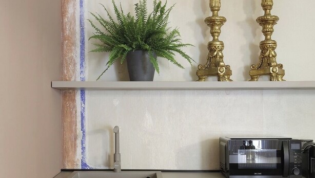 Une cuisine équipée d’un four à micro-ondes, d’une plante en pot et de deux chandeliers dorés décoratifs posés sur une étagère.