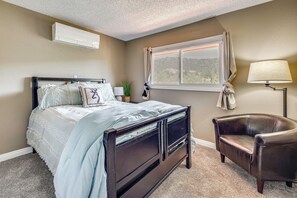 A bedroom with a bed, a chair, a window with curtains, a lamp, and an air conditioner. - Hiking Days, Fireside Nights! Colorado Springs Gem (Colorado Springs)