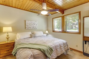 Une chambre à coucher comprenant un lit, une table de chevet, une lampe, un ventilateur de plafond, des œuvres d’art et des fenêtres.