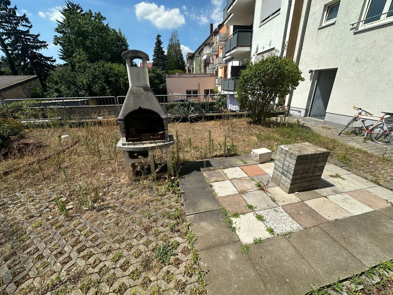 Een stenen barbecue, een geruit terras en een gebouw met balkons op de achtergrond.
