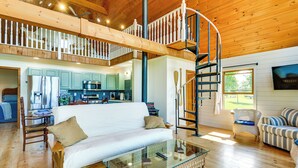 A spacious living area with a high ceiling, a glass coffee table, a sofa, a wicker chair, and a spiral staircase. - Fisherman's Retreat on Lake Ontario, Near Marina (Cape Vincent)