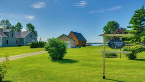 A well-maintained lawn with a wooden structure, a signboard, and a view of a lake. - Fisherman's Retreat on Lake Ontario, Near Marina (Cape Vincent)