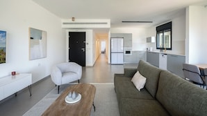 Un salon moderne comprenant un canapé, un fauteuil et une table basse, qui donne sur une cuisine et un coin repas.