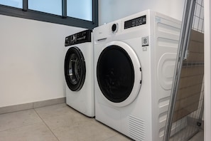 Two front-loading washing machines in a laundry room with a tiled floor and a window above. - Stylish 4BR Apt l Balcony & Mamad (Bat Yam)