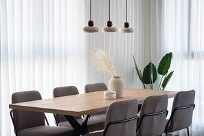 A dining area with a wooden table, six chairs, a vase with dried plants, and hanging pendant lights. - Stylish 4BR Apt l Balcony & Mamad (Rishon LeTsiyon)