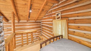 En stuga byggd av timmer med en säng, väggar av trä, en trätrappa och ett fönster med gardiner.