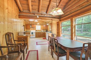 A wooden cabin interior with a dining area, kitchen, and large windows. - Pigeon River Escape Surrounded by State Land! (Vanderbilt)