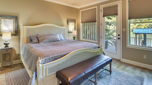 A bedroom with a bed, bench, ceiling fan, and large windows.