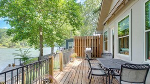 A wooden deck with outdoor furniture, a grill, and a view of a lake.