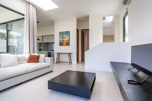 A modern living room with a sofa, a coffee table, and a flat-screen TV. There is a staircase leading to an upper level. - VOX Residences Canggu (Bali)