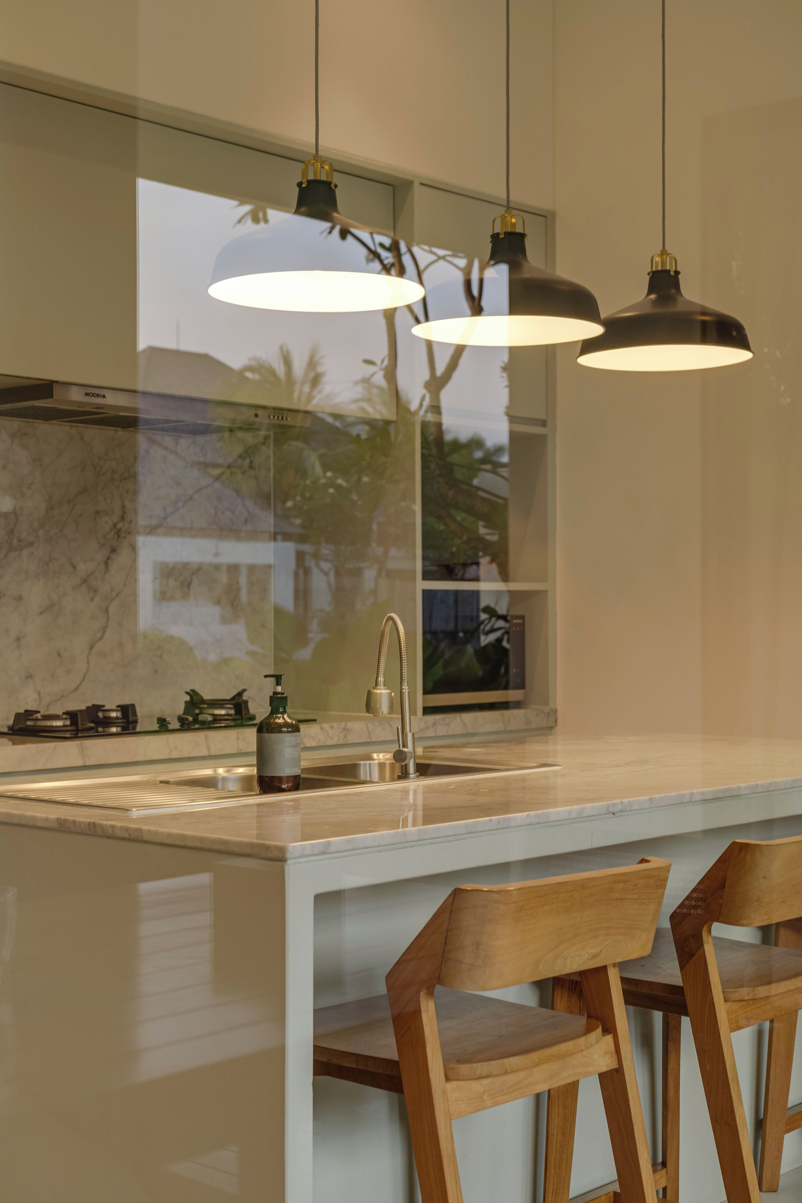 A modern kitchen with a marble countertop, stainless steel sink, and wooden chairs.