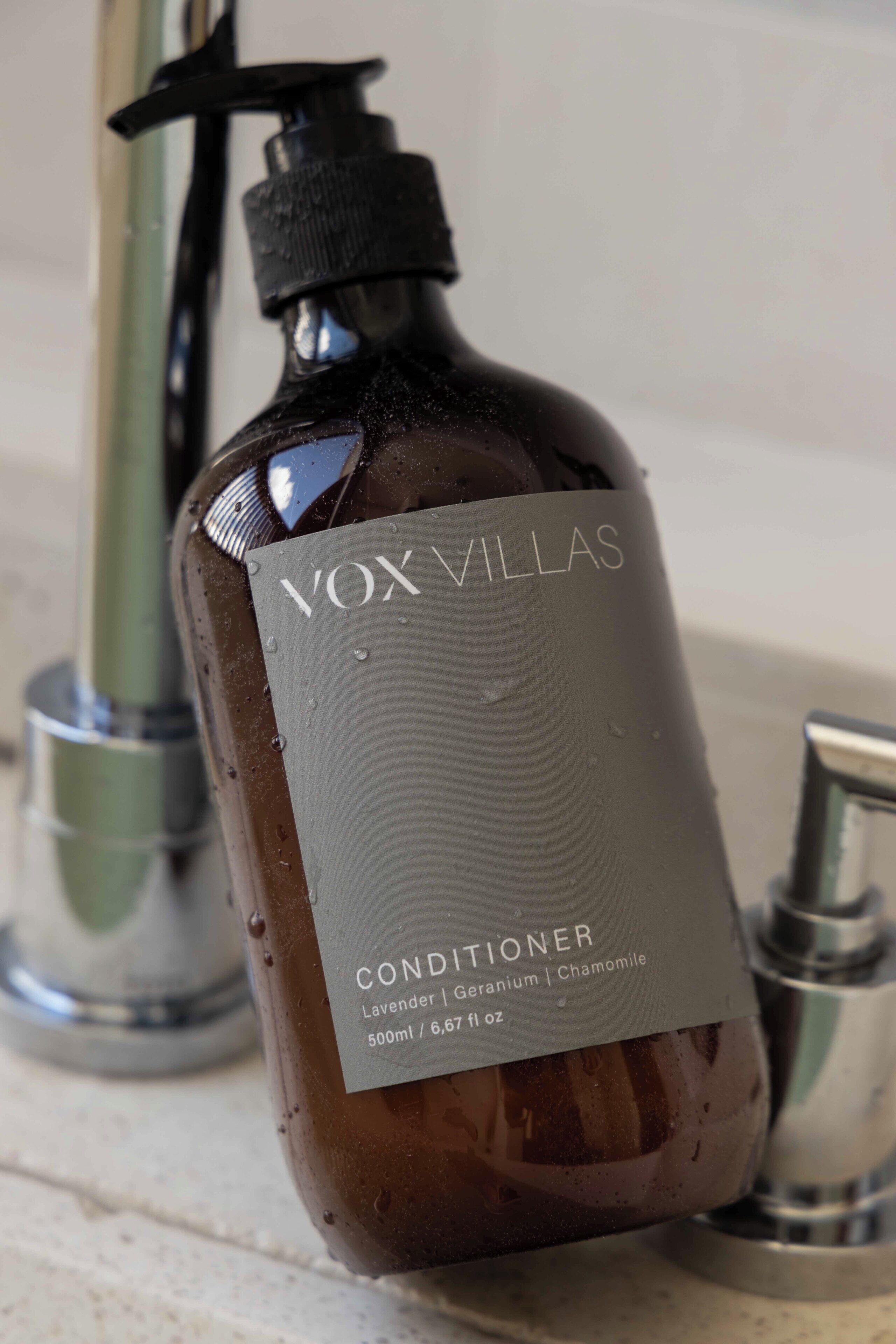 Una botella de acondicionador VOX VILLAS con dosificador tipo bomba, sobre una encimera de baño.