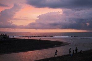 Escena de playa con gente, una costa curvada y un atardecer.