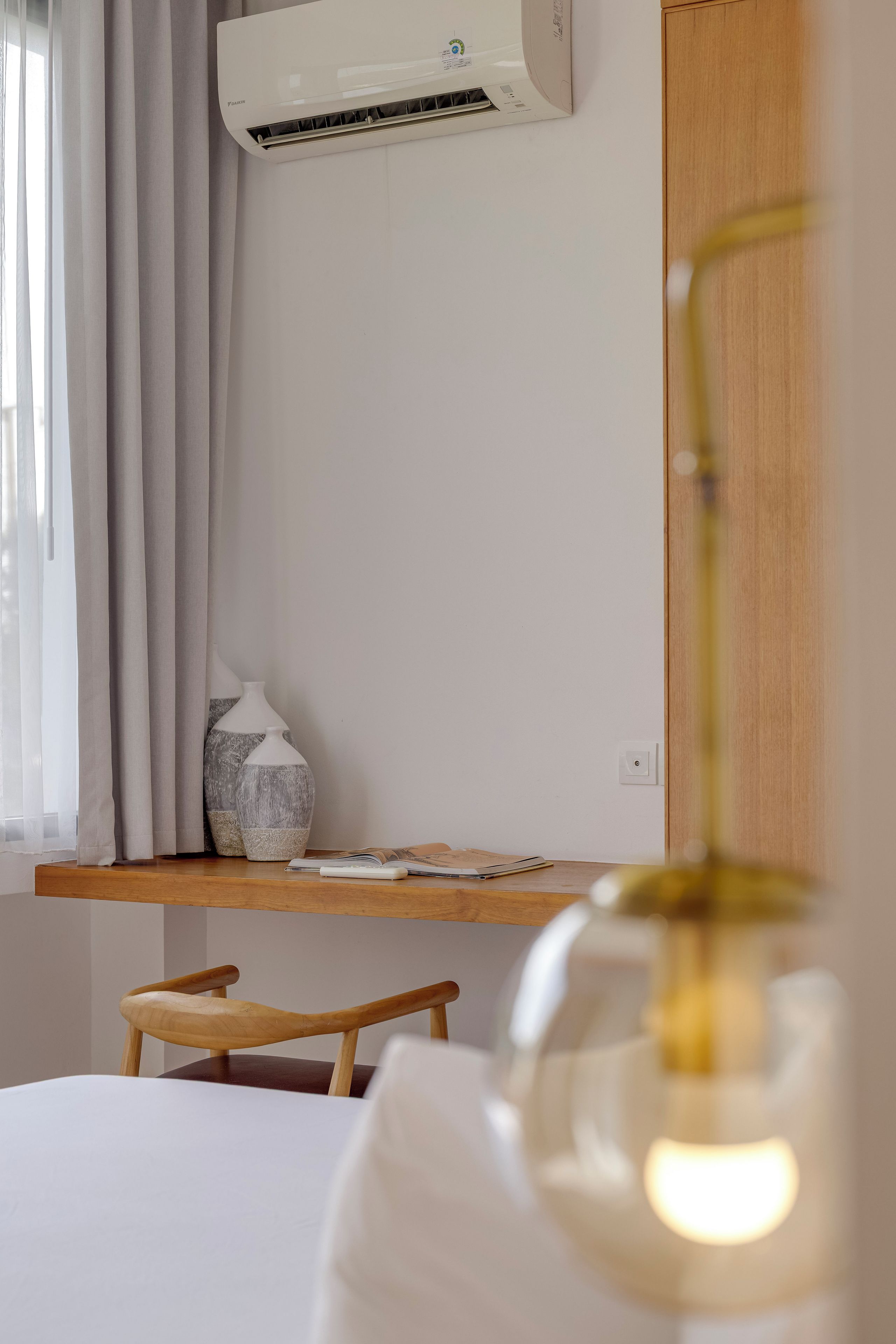 Une chambre avec un lit, une table de chevet en bois, un vase blanc et un appareil de climatisation fixé au mur.