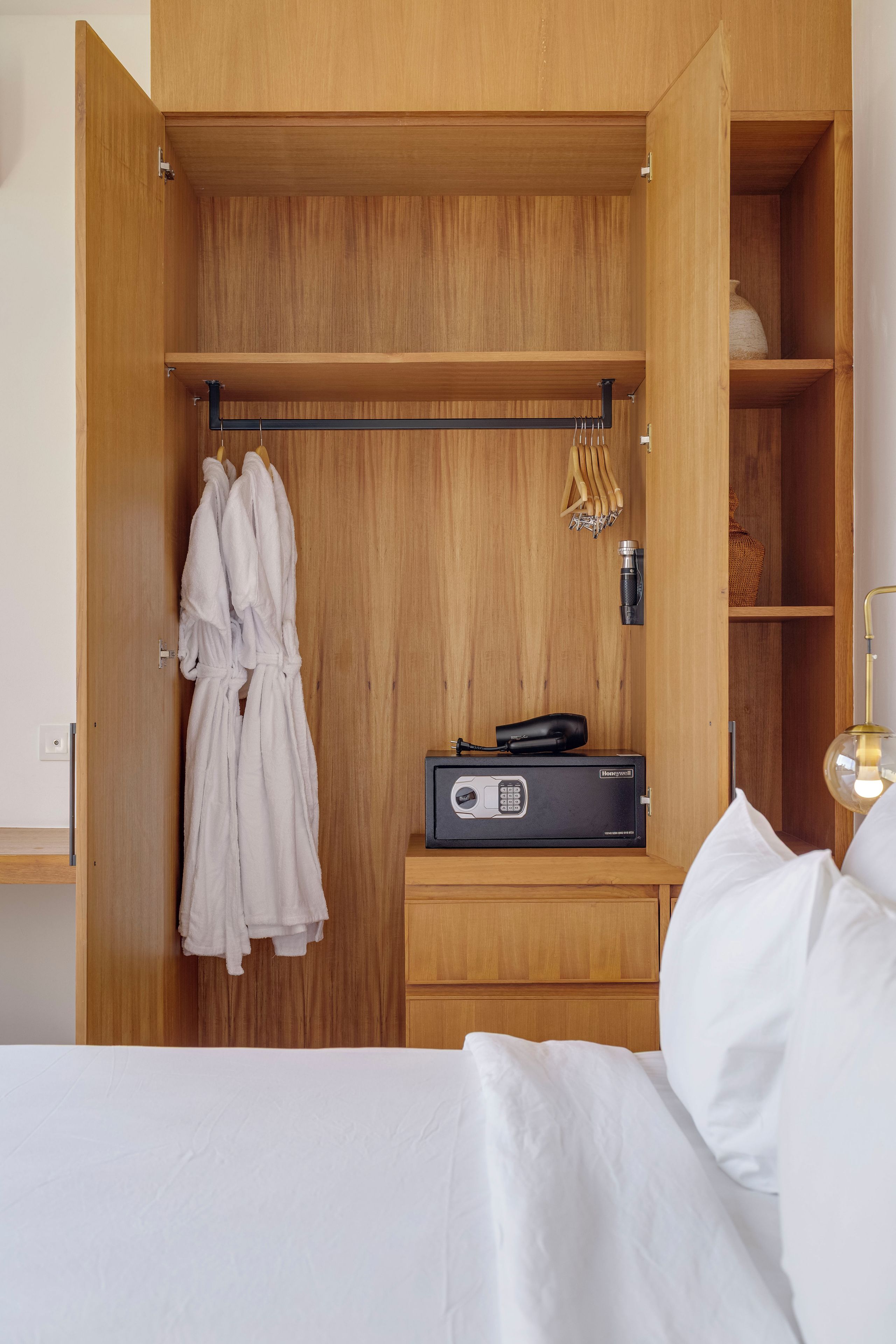 A wooden wardrobe with a hanging rack, a safe, and a bed with white bedding.