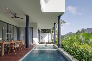 A modern outdoor pool area with a wooden deck, seating, and a view of the surrounding landscape.