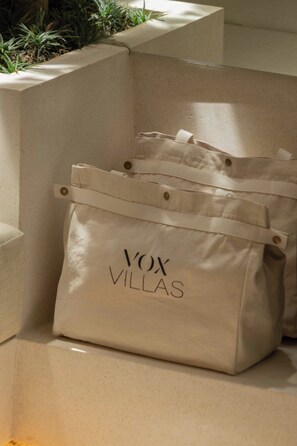 Eine beige Tasche aus Leinwand mit dem Aufdruck 'VOX VILLAS', platziert auf einer Betonstufe.