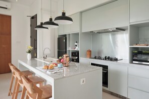 Una cocina moderna con una isla central, taburetes de bar, iluminación colgante y electrodomésticos de acero inoxidable.