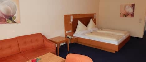 Habitación de hotel con cama, sofá, sillón, una mesita y dos cuadros en las paredes.