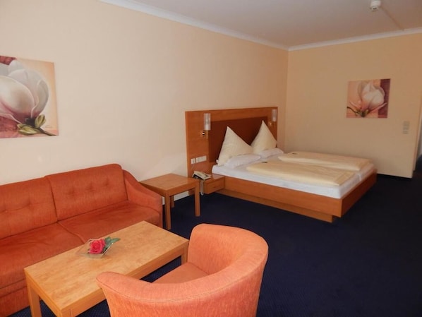 A hotel room with a bed, a sofa, a chair, a small table, and two paintings on the walls.