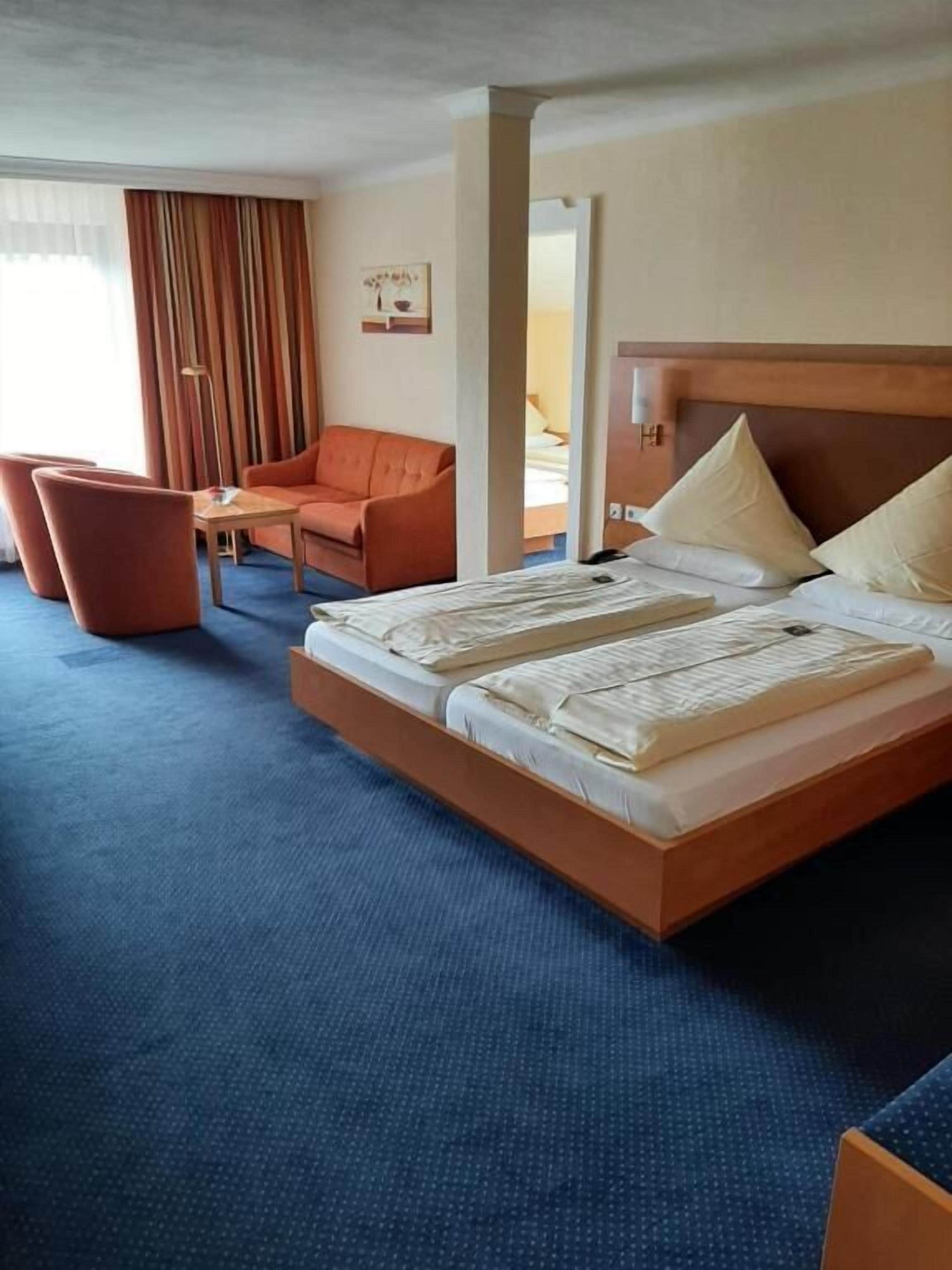 A hotel room with a large bed, a sofa, a small table, and a window with curtains.