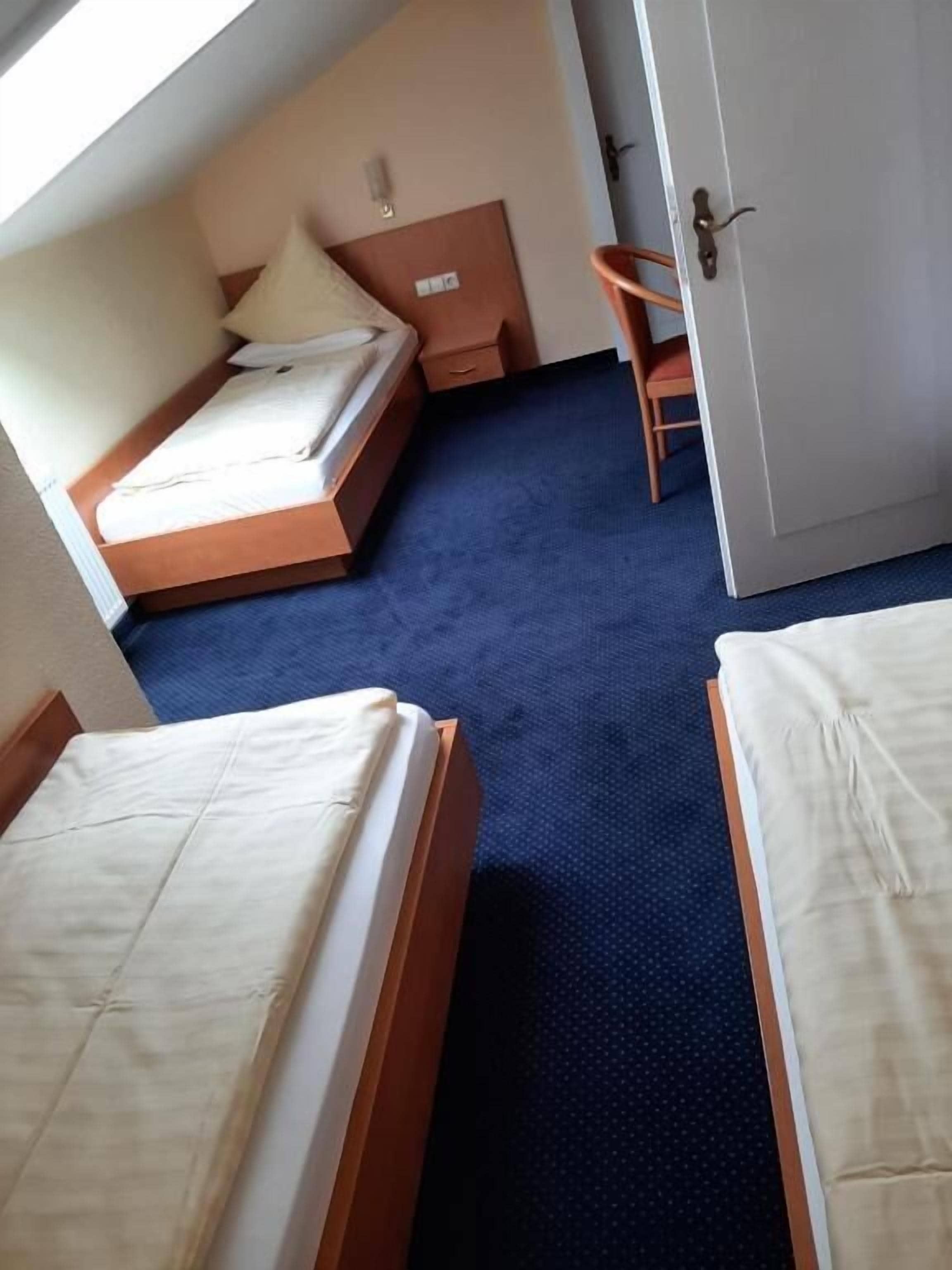 A room with two beds, a wardrobe, a chair, and a small table.