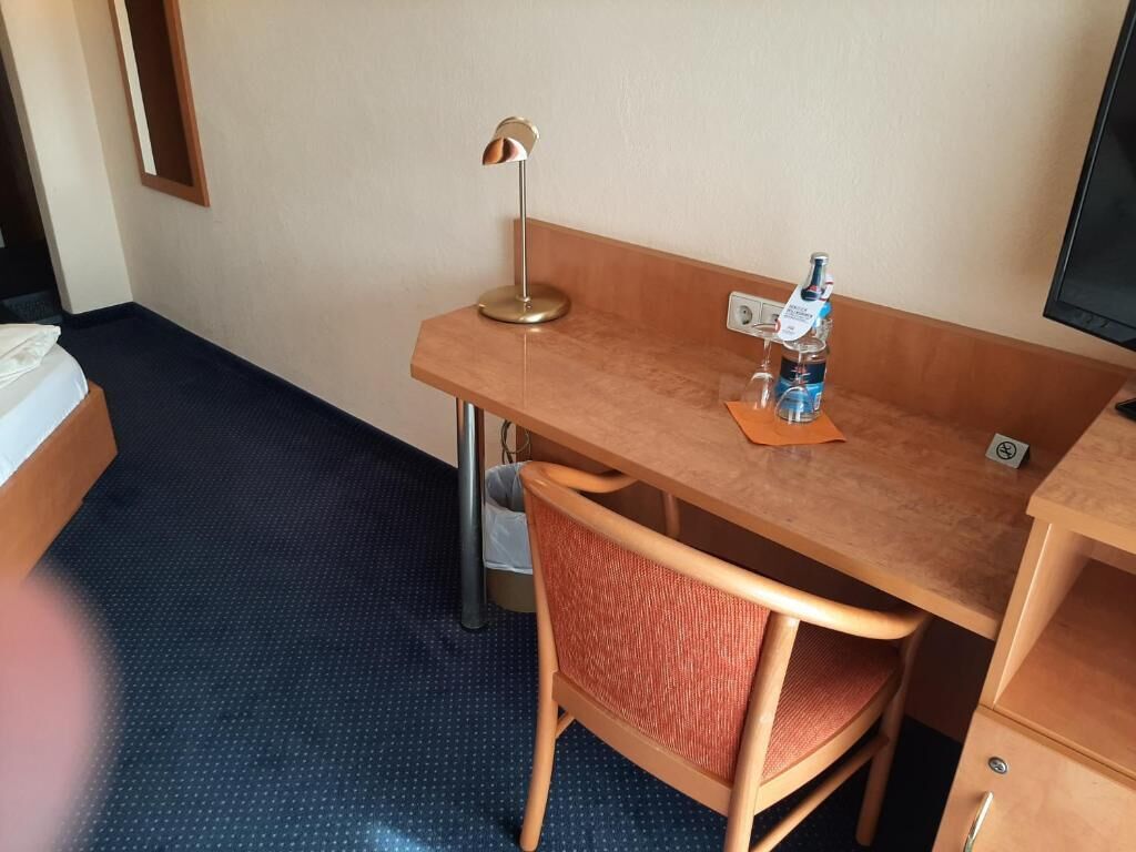 A hotel room with a wooden desk, a chair, a lamp, a bottle of water, and a TV.