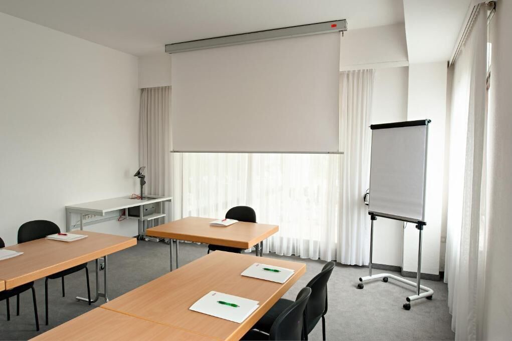 A conference room with a whiteboard, a projector screen, and a desk with a lamp.