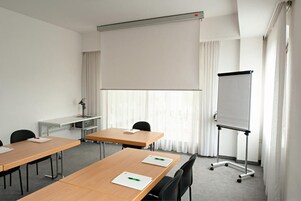 Un salón de conferencias con una pizarra, una pantalla de proyector y un escritorio con una lámpara.