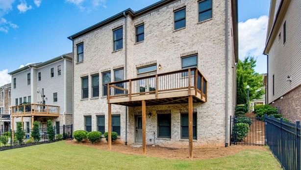 A multi-story residential building with a brick facade, a covered outdoor area with a wooden deck, and a fenced yard. - Executive 5BR Stay in Duluth w/ Pool Access (Duluth)