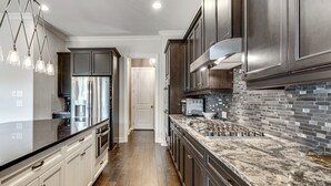 A modern kitchen with stainless steel appliances, dark cabinetry, and a marble countertop. - Executive 5BR Stay in Duluth w/ Pool Access (Duluth)