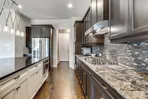 A modern kitchen with stainless steel appliances, dark cabinetry, and a marble countertop. - Executive 5BR Stay in Duluth w/ Pool Access (Duluth)