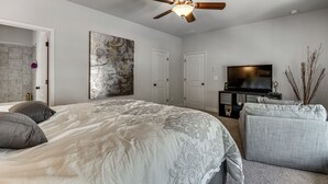 A bedroom with a large bed, a ceiling fan, a flat-screen TV, and a decorative wall piece. - Executive 5BR Stay in Duluth w/ Pool Access (Duluth)
