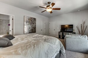 A bedroom with a large bed, a ceiling fan, a flat-screen TV, and a decorative wall piece. - Executive 5BR Stay in Duluth w/ Pool Access (Duluth)