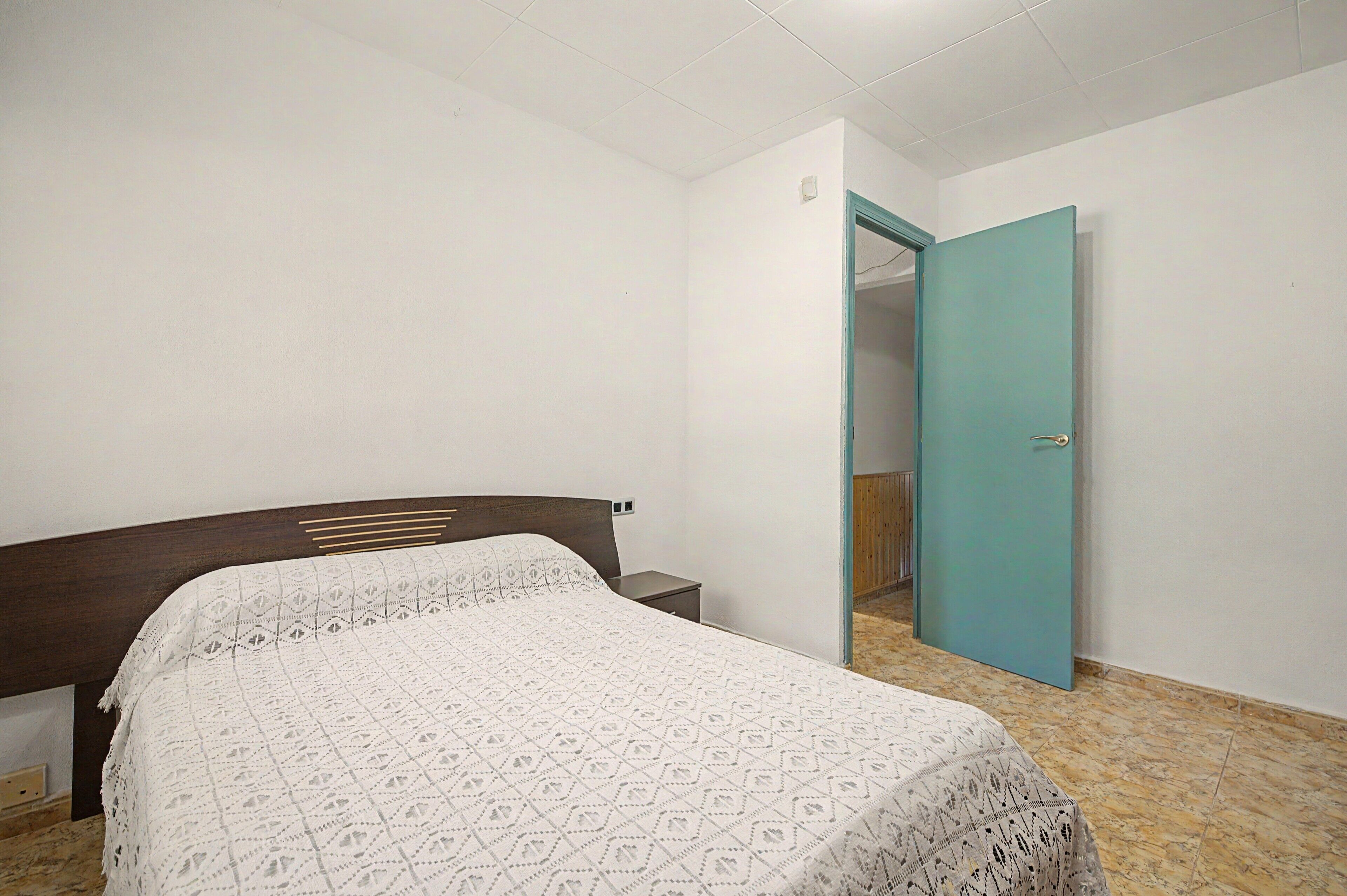 Ein Schlafzimmer mit Bett, Nachttisch, Tür und Fliesenboden.
