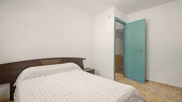 Ein Schlafzimmer mit Bett, Nachttisch, Tür und Fliesenboden.