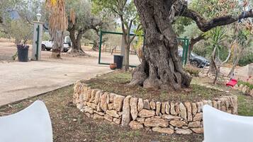 Un muro de piedra, un árbol grande y una silla de plástico blanca.