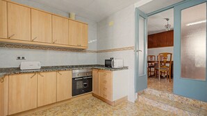 A compact kitchen with wooden cabinets, a built-in oven, a microwave, and a dining area with a table and chairs.