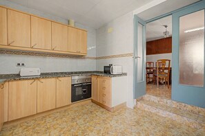 A compact kitchen with wooden cabinets, a built-in oven, a microwave, and a dining area with a table and chairs.
