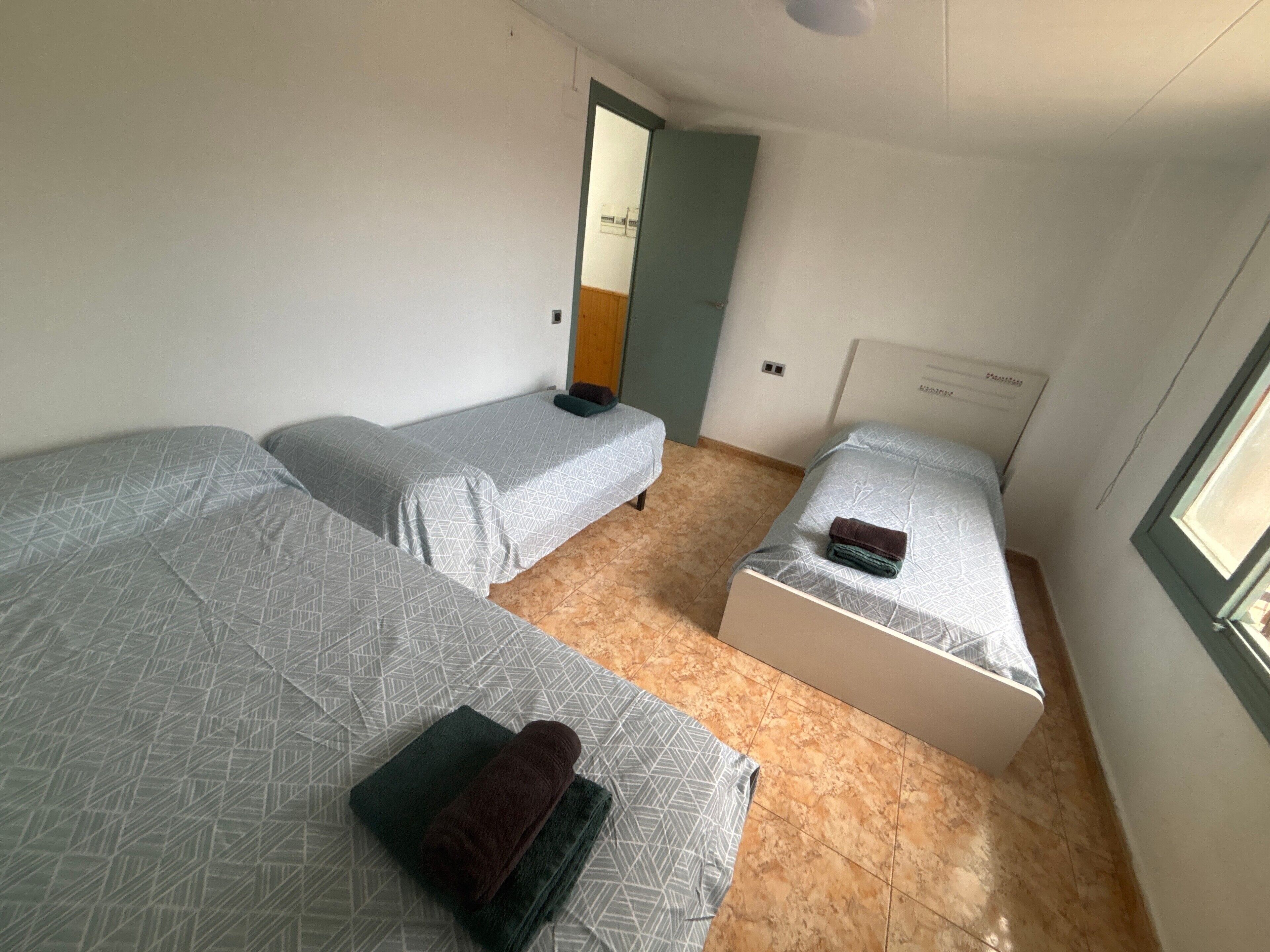 Una habitación pequeña y limpia con dos camas individuales, una puerta y una ventana.