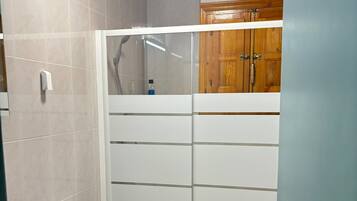 A bathroom with a toilet, a shower enclosure, and a wooden cabinet.