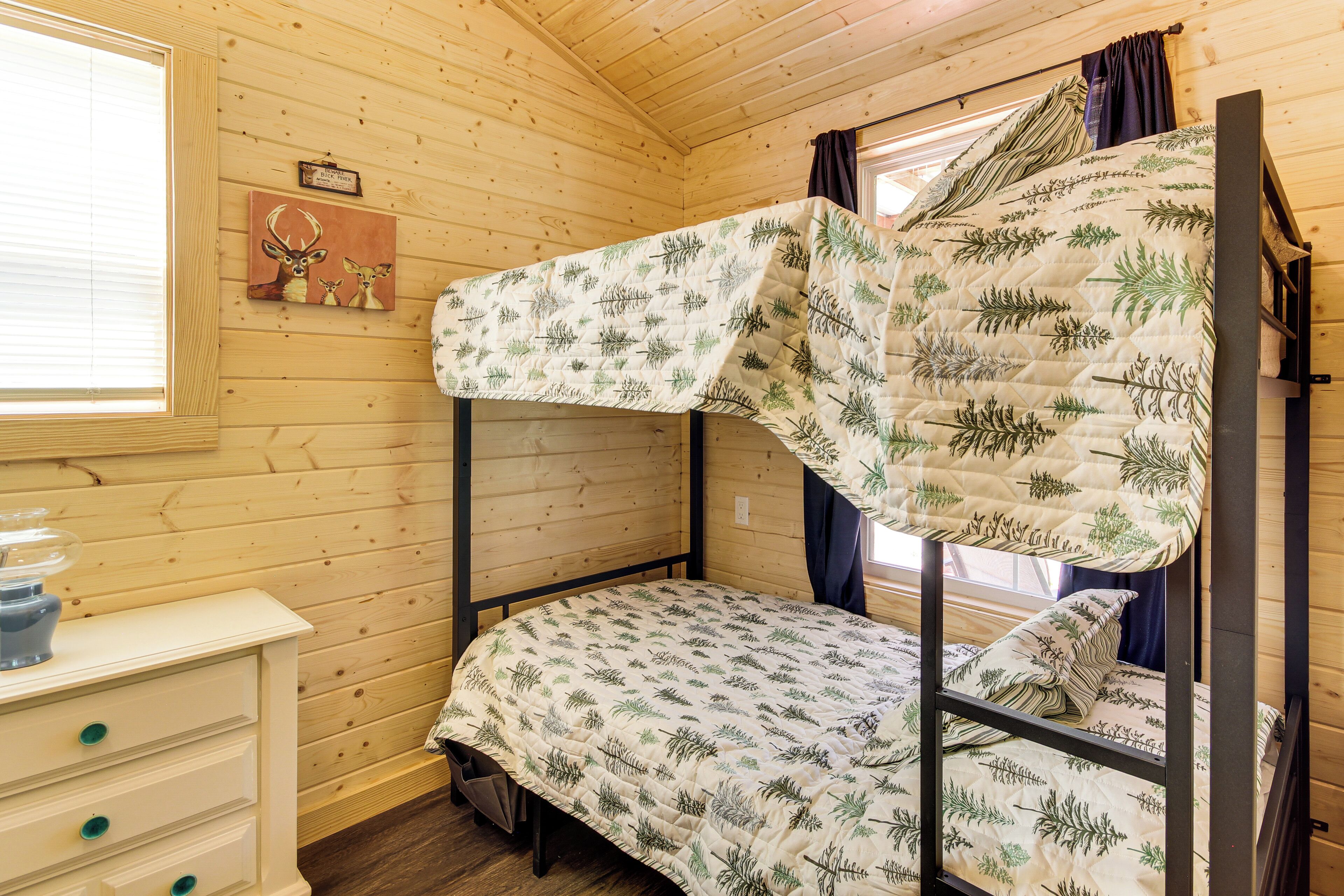 A bunk bed with a leaf-patterned quilt, a wooden dresser with drawers, and a window with blinds.