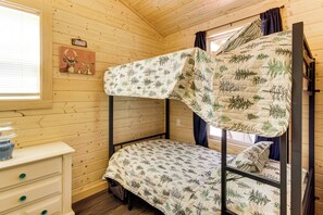 Ein Etagenbett mit einem Bettbezug mit Blättermotiv, eine Holzkommode mit Schubladen und ein Fenster mit Jalousien.