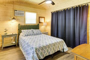 A wooden room with a bed, a nightstand, a lamp, a window with blinds, and a curtain. - Cabin is 2 Miles From Bogue Chitto State Park (Franklinton)