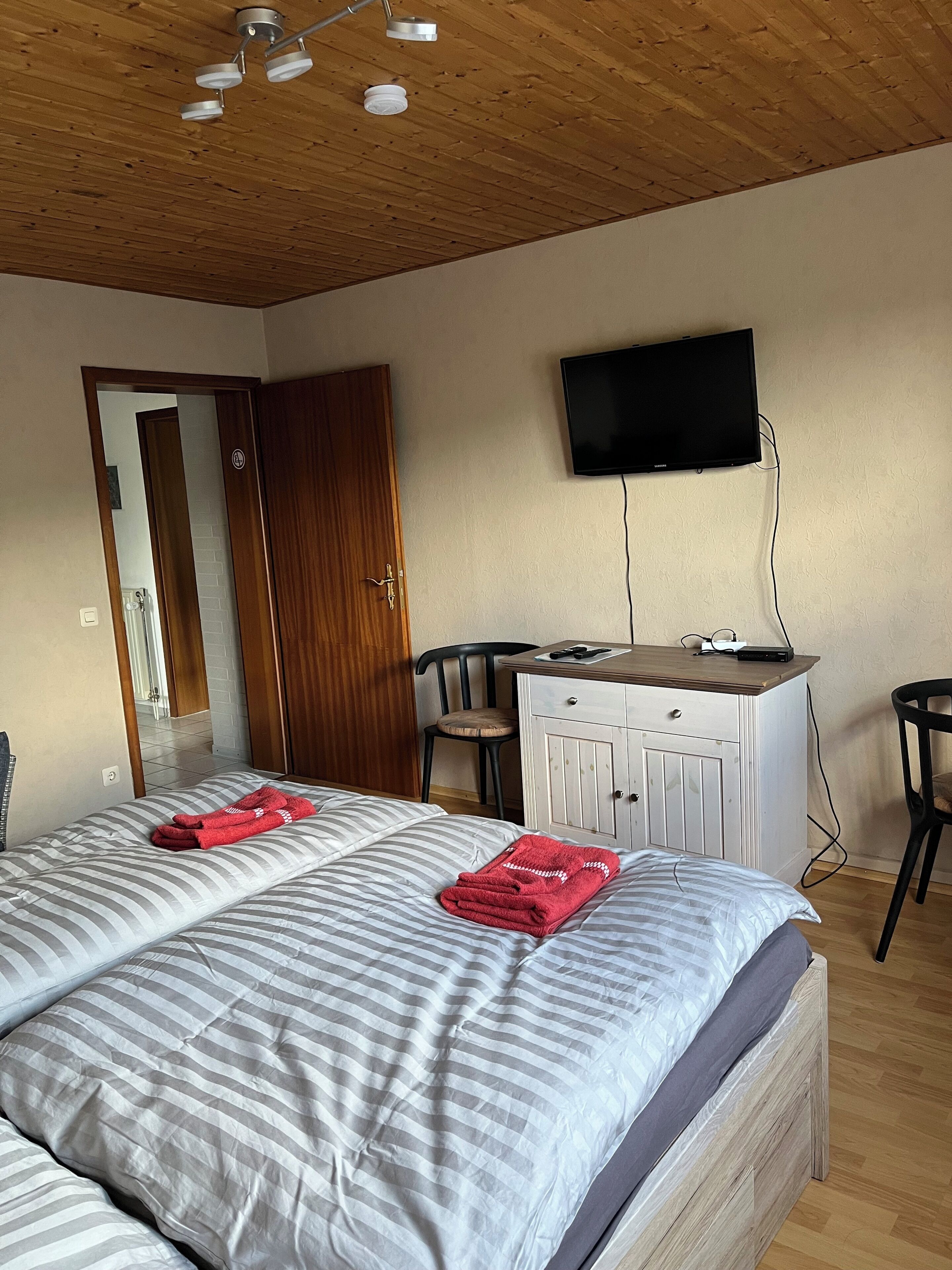Ein Hotelzimmer mit einem Bett, einem Schreibtisch, einem Sessel, einem Fernseher und einer Holzbalkendecke.
